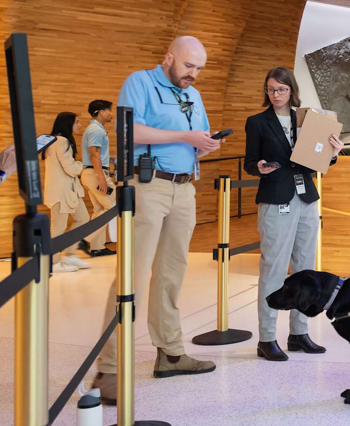 A group of visitors, including two accompanied by service dogs and one using a cane, in line to present their tickets to a staff member in the Museum of Exploration's lobby.