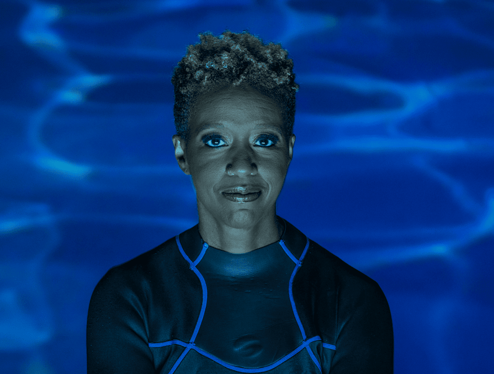 A headshot of National Geographic Explorer Tara Roberts, dressed in a wet suit in from of a ambient ocean background