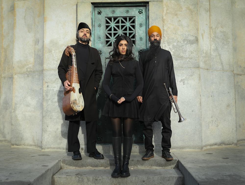 A musical trio standing in front of a stone building.