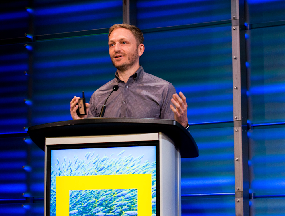 A man speaking at a National Geographic Podium.