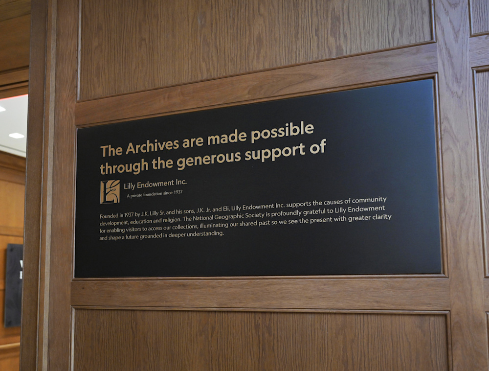 A large matte black placard inset on a beautiful wooden wall includes large title text thanking Lilly Endowment Inc. for their generous support of The Archives exhibition.