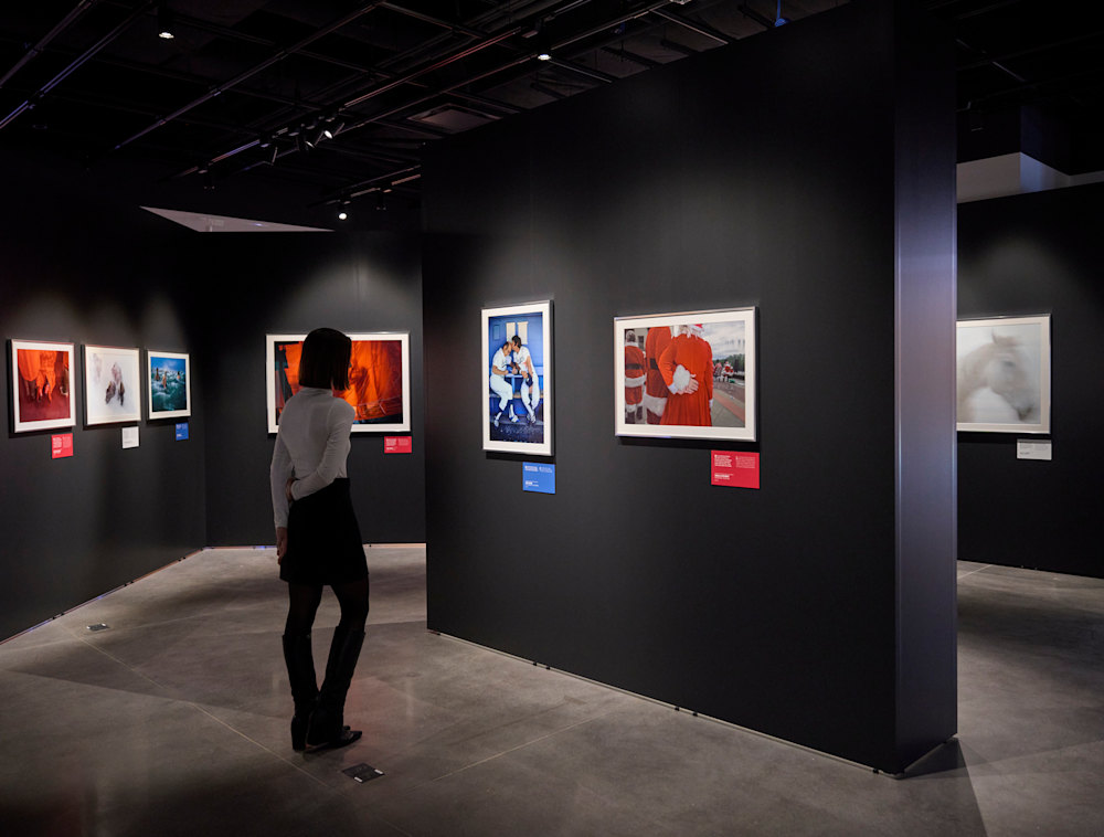 A gallery visitor examines framed photography and printed descriptions on the walls of the "Red, White & Blue" exhibition.