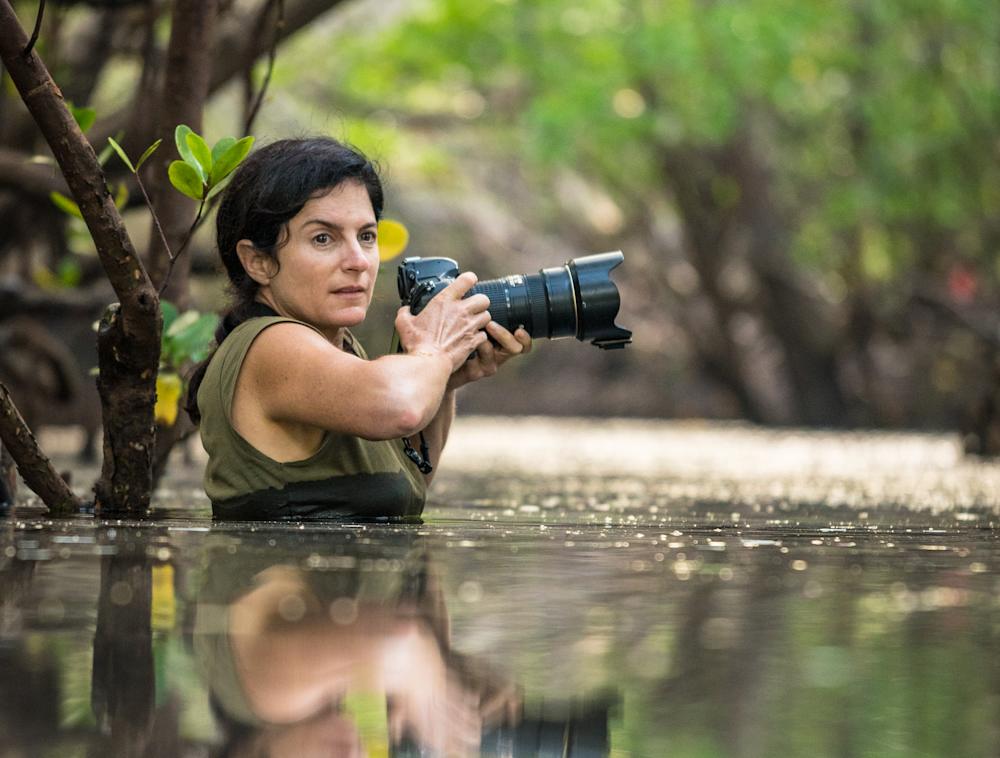 National Geographic Explorer Ami Vitale taking photographs in the field while waist deep in water. 