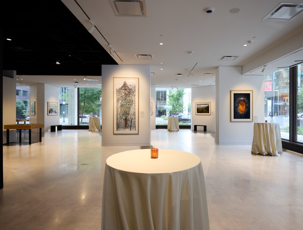 Tall, event tables with white tablecloths in an emtpy photography gallery. 