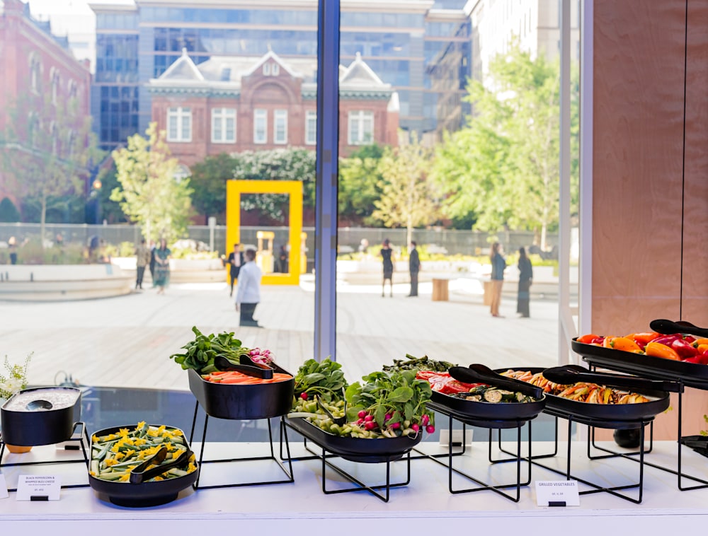 A buffet table laid with oblong serving dishes filled with food. Behind the table, a window looks out onto the courtyard with its giant yellow rectangle statue.