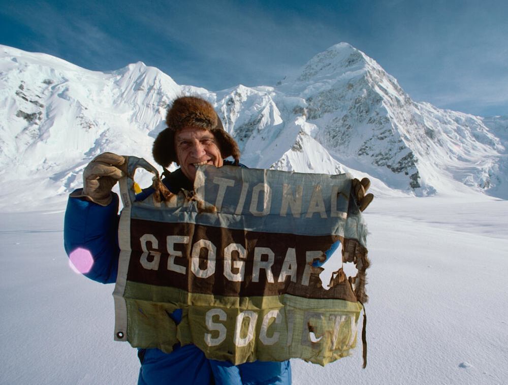 In the snowy mountains holding up the National Geographic Society flag.