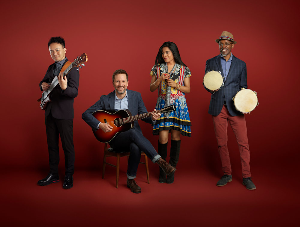Four musicians posing together against a red background.