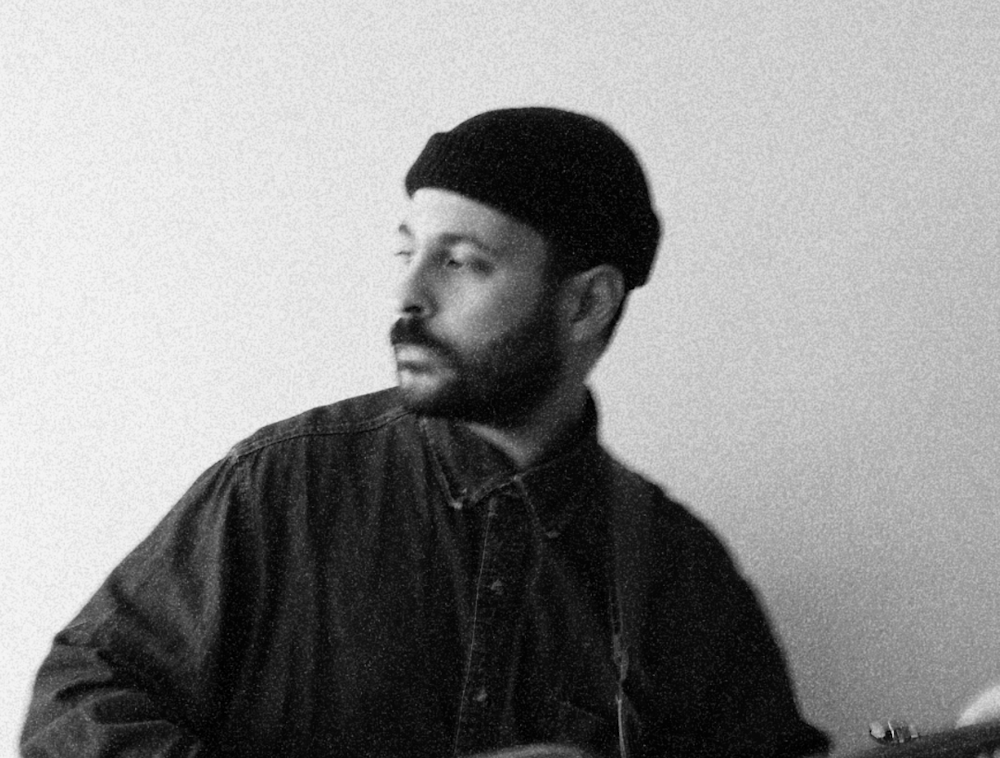 Nour Harkati holding his guitar in a black and white photo.