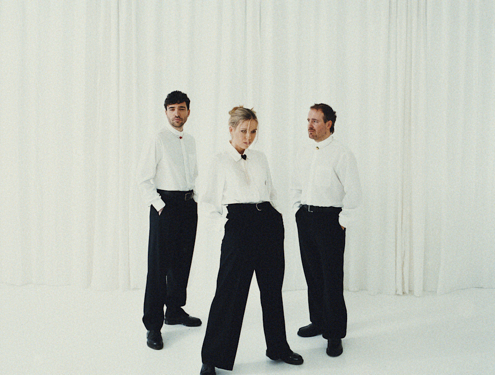Three individuals standing together against a backdrop of white curtains.