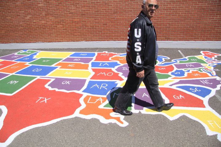 Photograph of man walking over U.S. map chalk drawing on sidewalk.