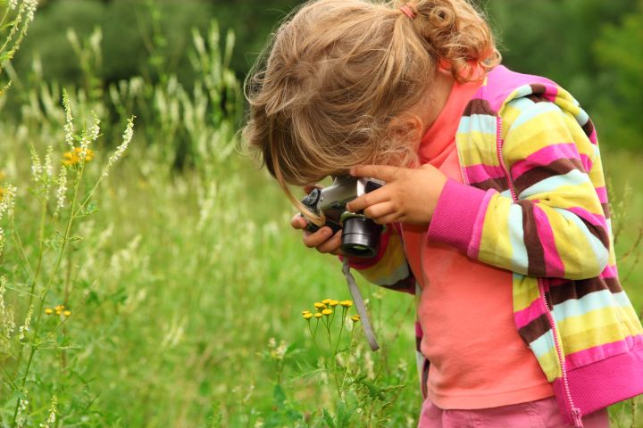 Little girl photographs flower outdoors