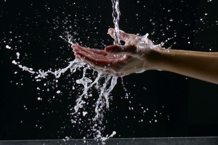 A photograph of hands being washed with soap under a stream of water.