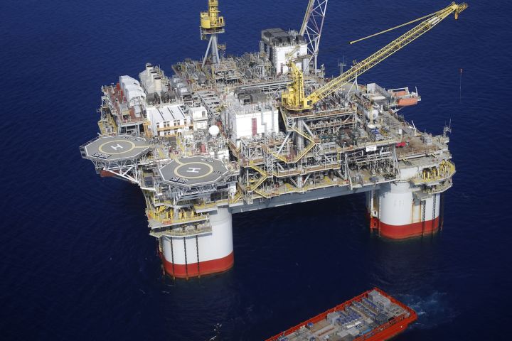 A large ship sits off the side of an offshore oil platform