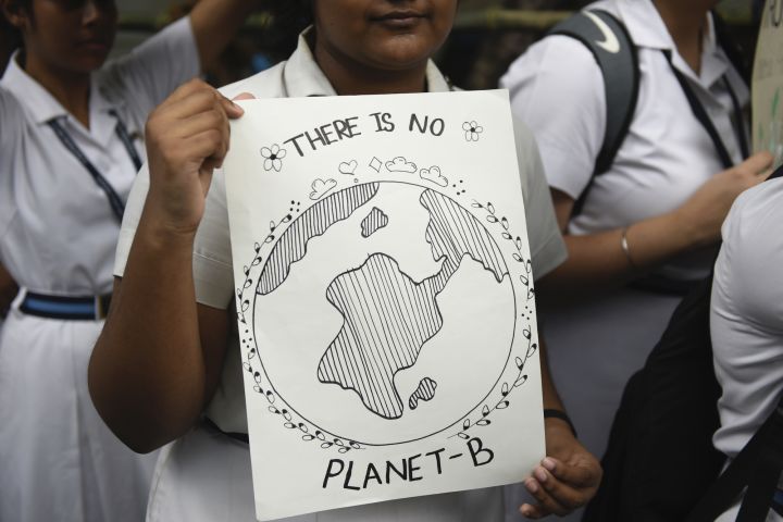 Image of a student at a protest holding a black and white hand drawn poster with Earth in the center and the text there is no planet b on it.