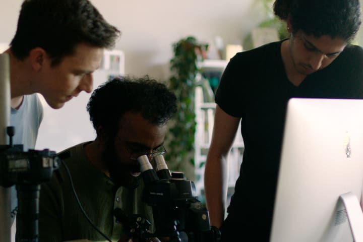 Photograph of three scientists making observations through a microscope.