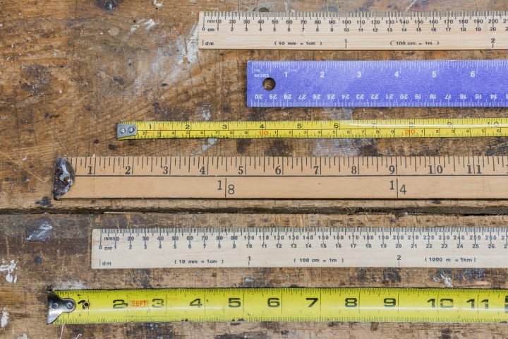 Six measuring sticks placed horizontally on a wooden board.