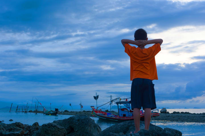 Photograph of a child looking up at a cloudy sky along the coast.