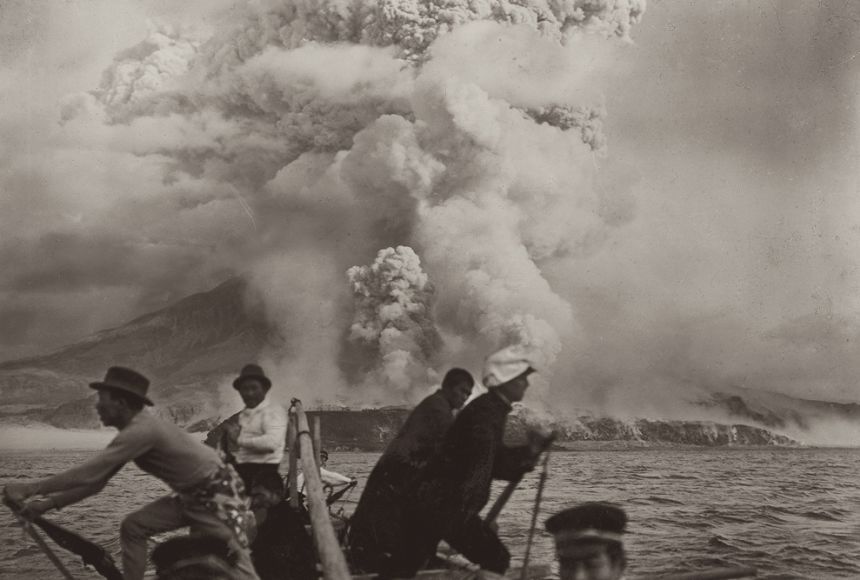 Black-and-white photo of men in a boat fleeing a volcano.