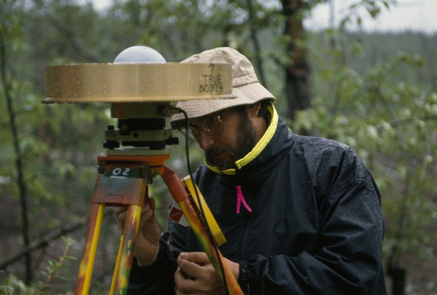 Scientist Doug Caprette ventures out in the rain to remove a GPS sensor from its spot on a USGS benchmark in the woods of McCarthy, Alaska, where it had been gathering data for a study on regional deformation caused by tectonic movements.