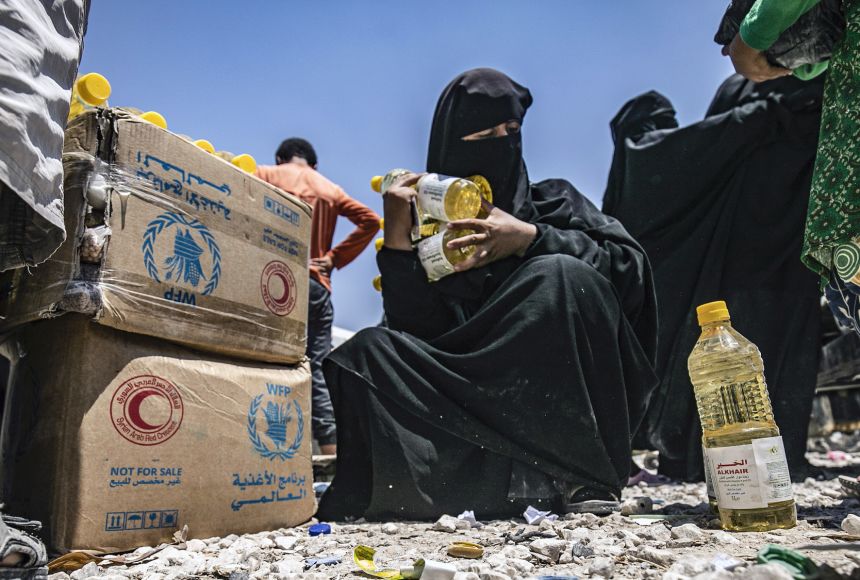 Intentional starvation has been used as a military tactic in the Syrian conflict. A woman is shown receiving food aid at al-Hol camp in Syria.