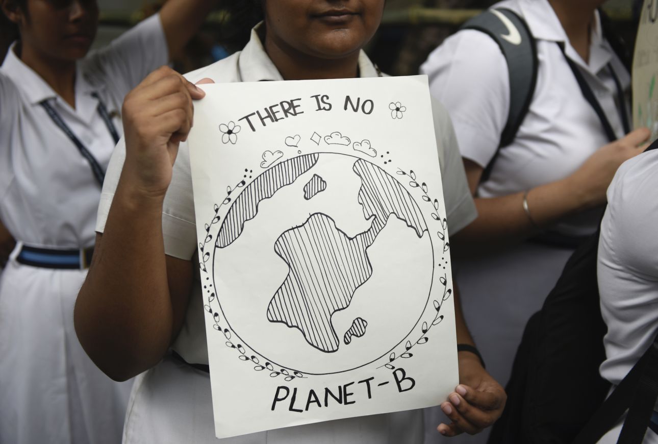Image of a student at a protest holding a black and white hand drawn poster with Earth in the center and the text there is no planet b on it.